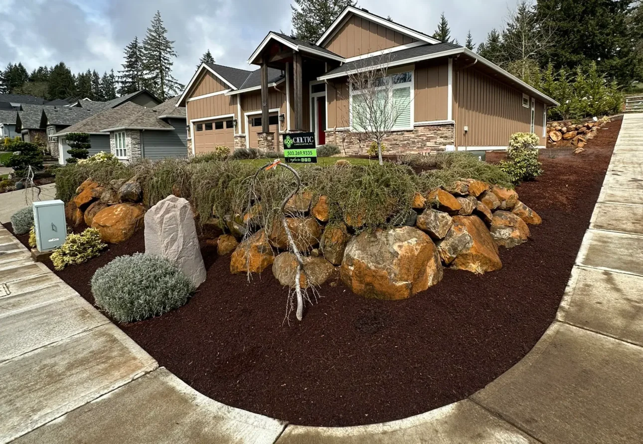 Residential front yard landscaping with natural boulders, mulch beds, and stone accents