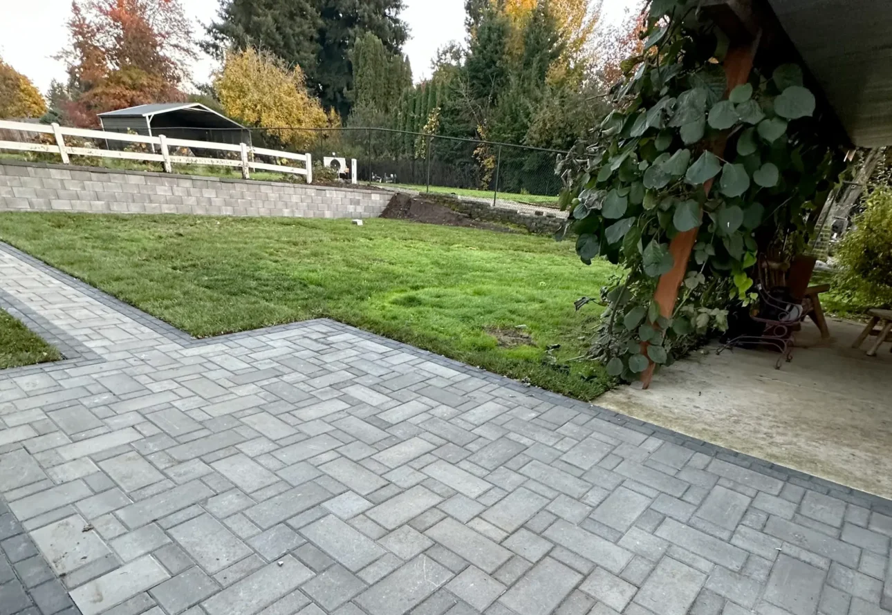 Backyard landscaping with paver patio, newly installed lawn, and retaining wall