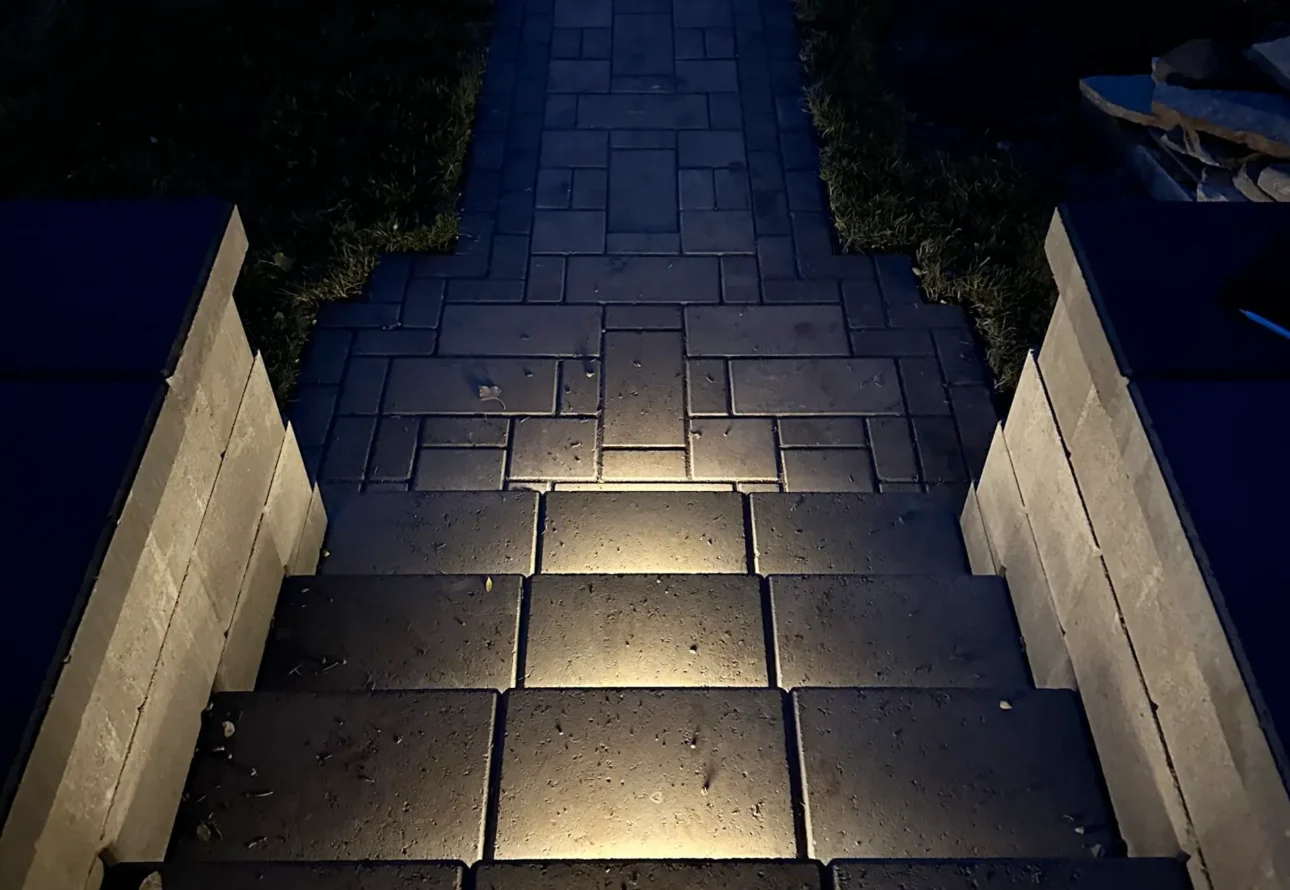 Outdoor paver steps with built-in lighting leading to a landscaped walkway at night