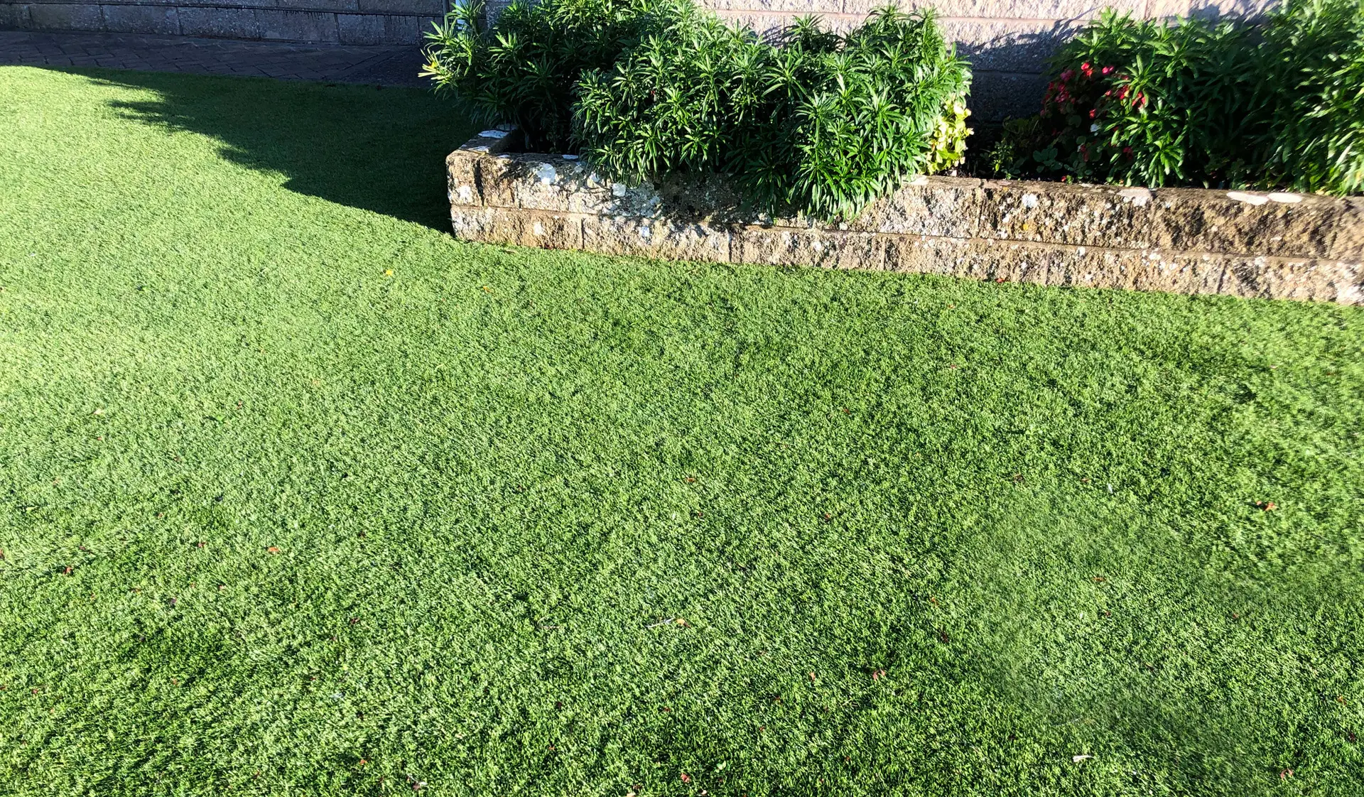 Artificial grass installation on a landscaped slope with stone retaining wall