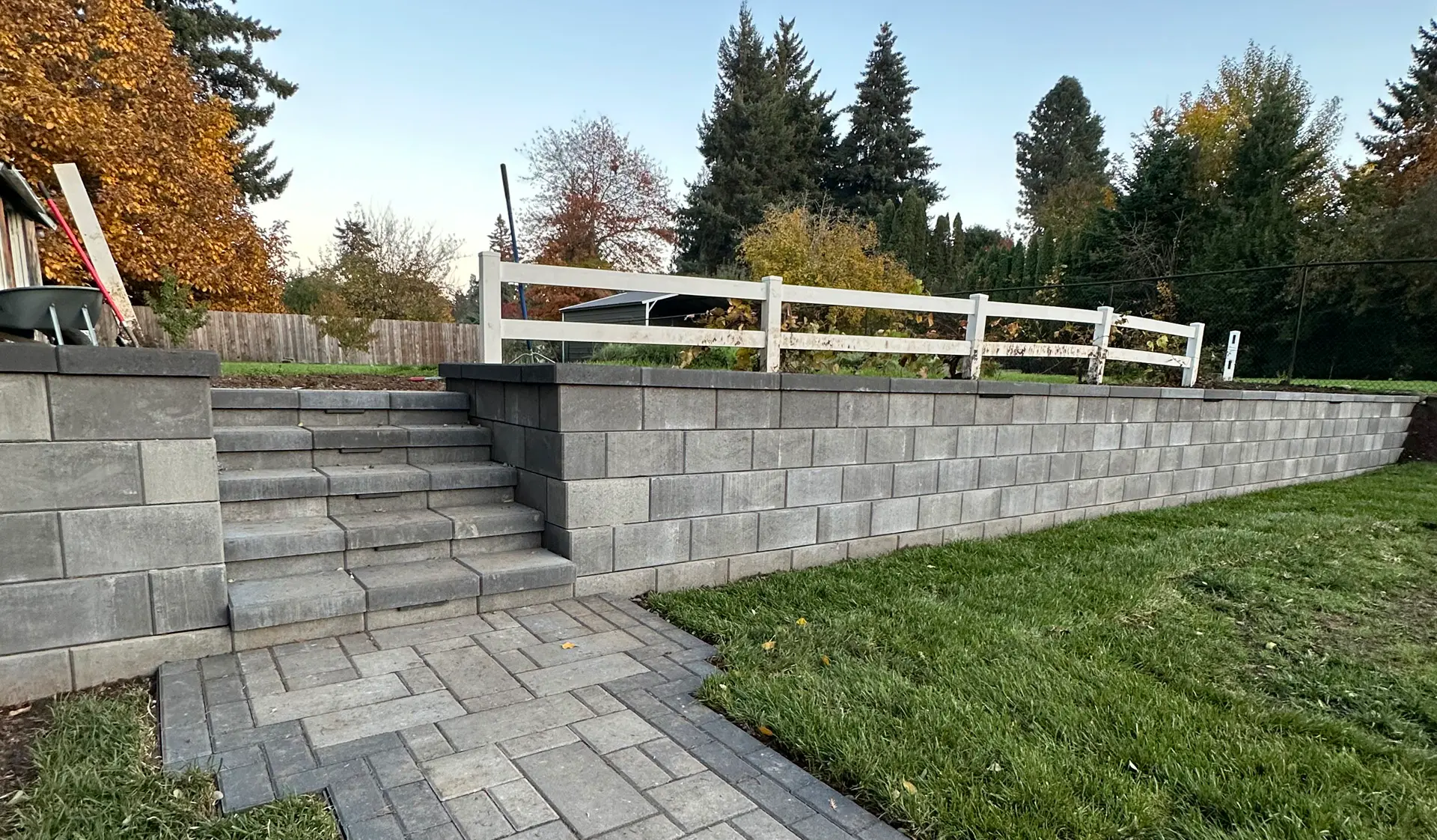 Retaining wall with stone steps leading to an upper yard area, featuring paver walkway and manicured lawn